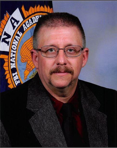 Ravalli County Sheriff Steve Holton in a suit jacket with a national academy insignia behind him
