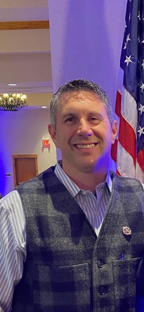 Gallatin County Undersheriff Jeremy Kopp wearing a wool vest with an American Flag in the background